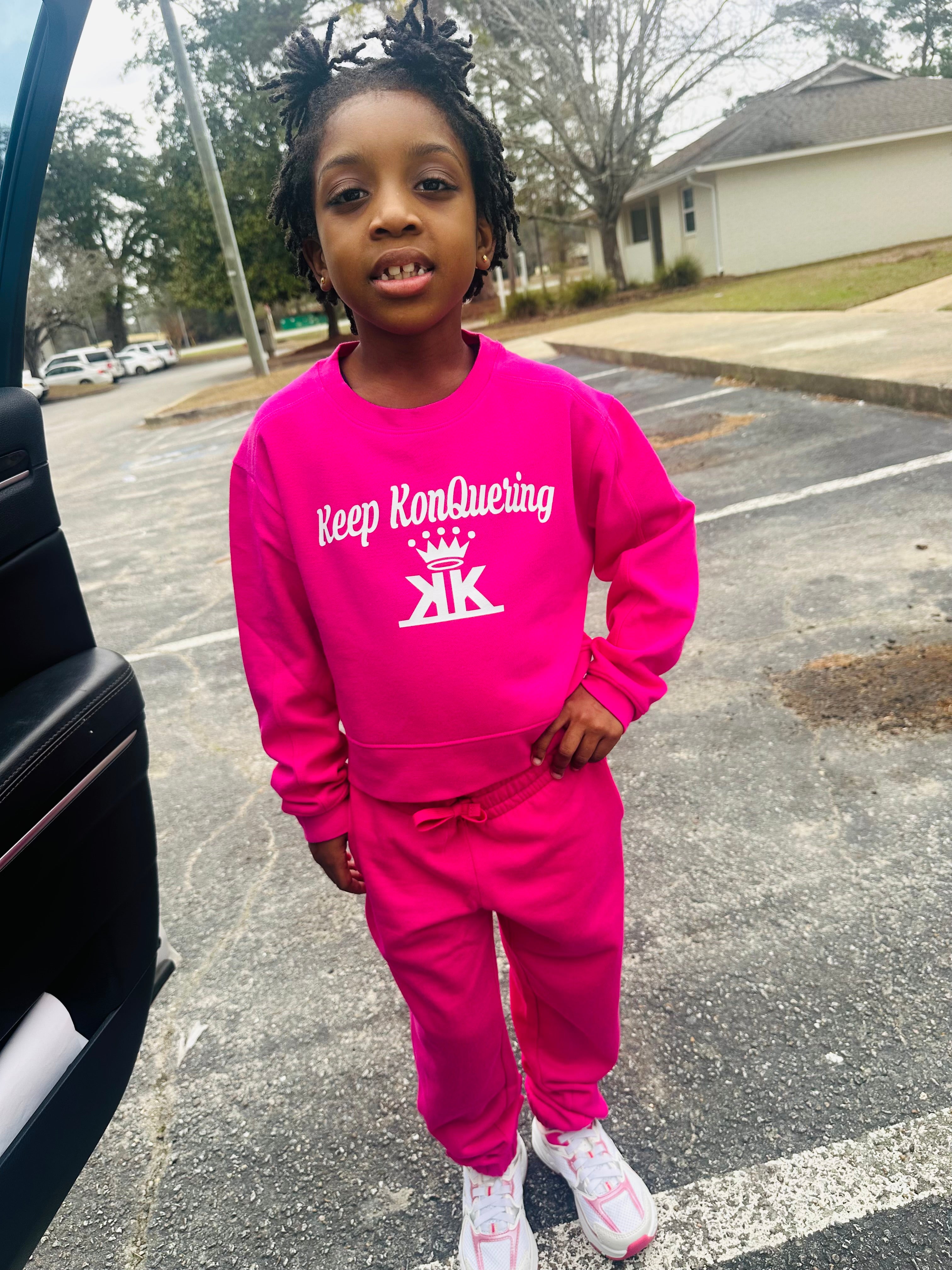 Child wearing a pink outfit with 'Keep Konquering' text in a parking lot.